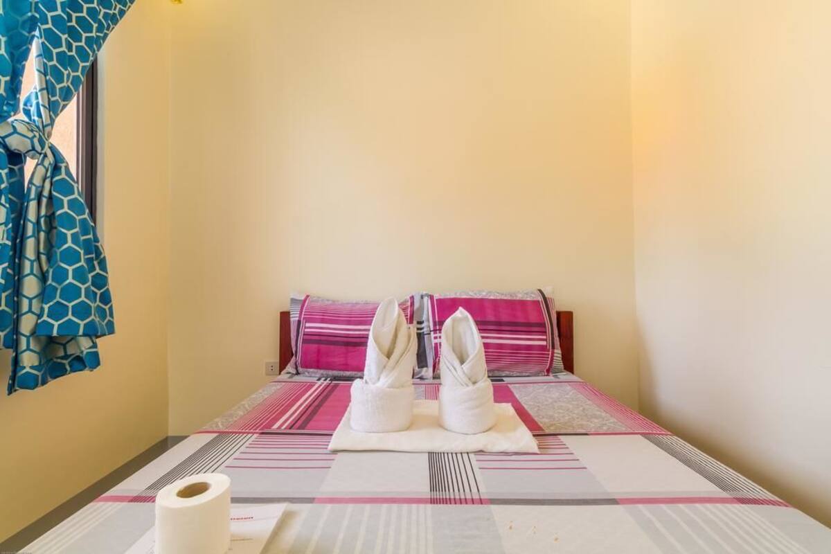 Une chambre d’hôtel avec un lit, des oreillers, un porte-serviettes et une fenêtre avec des rideaux.