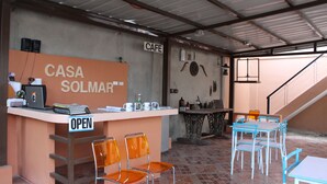 Ett café med en skylt som visar texten ”CASA SOLMAR” och en skylt som visar ”ÖPPET”. Det finns orangefärgade stolar och ett bord med blå stolar.