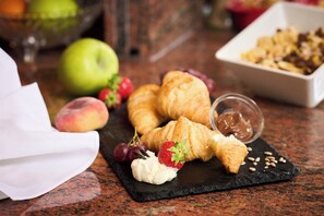 Un desayuno con cruasanes, fresas, uvas y un recipiente pequeño de mermelada sobre una tabla de pizarra.