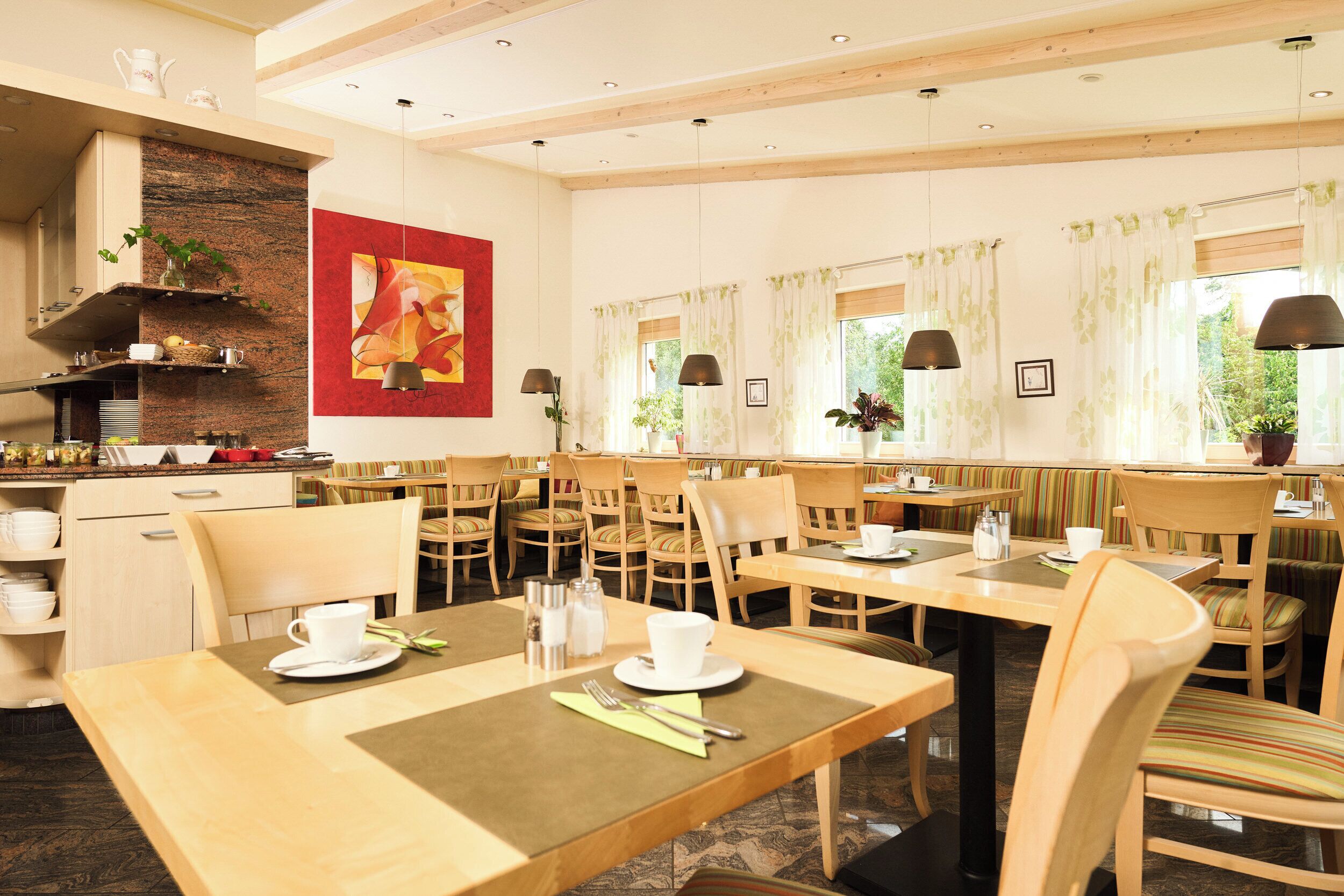 A dining area with multiple tables and chairs, a kitchen area with a brick wall, and a large painting on the wall.
