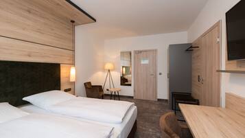 Una habitación de hotel moderna con dos camas, un escritorio, una silla, una lámpara y un espejo.