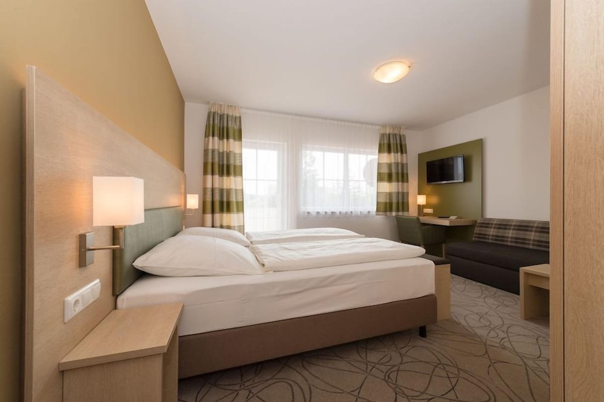 Una habitación de hotel con cama, mesitas de noche, televisor y sofá.