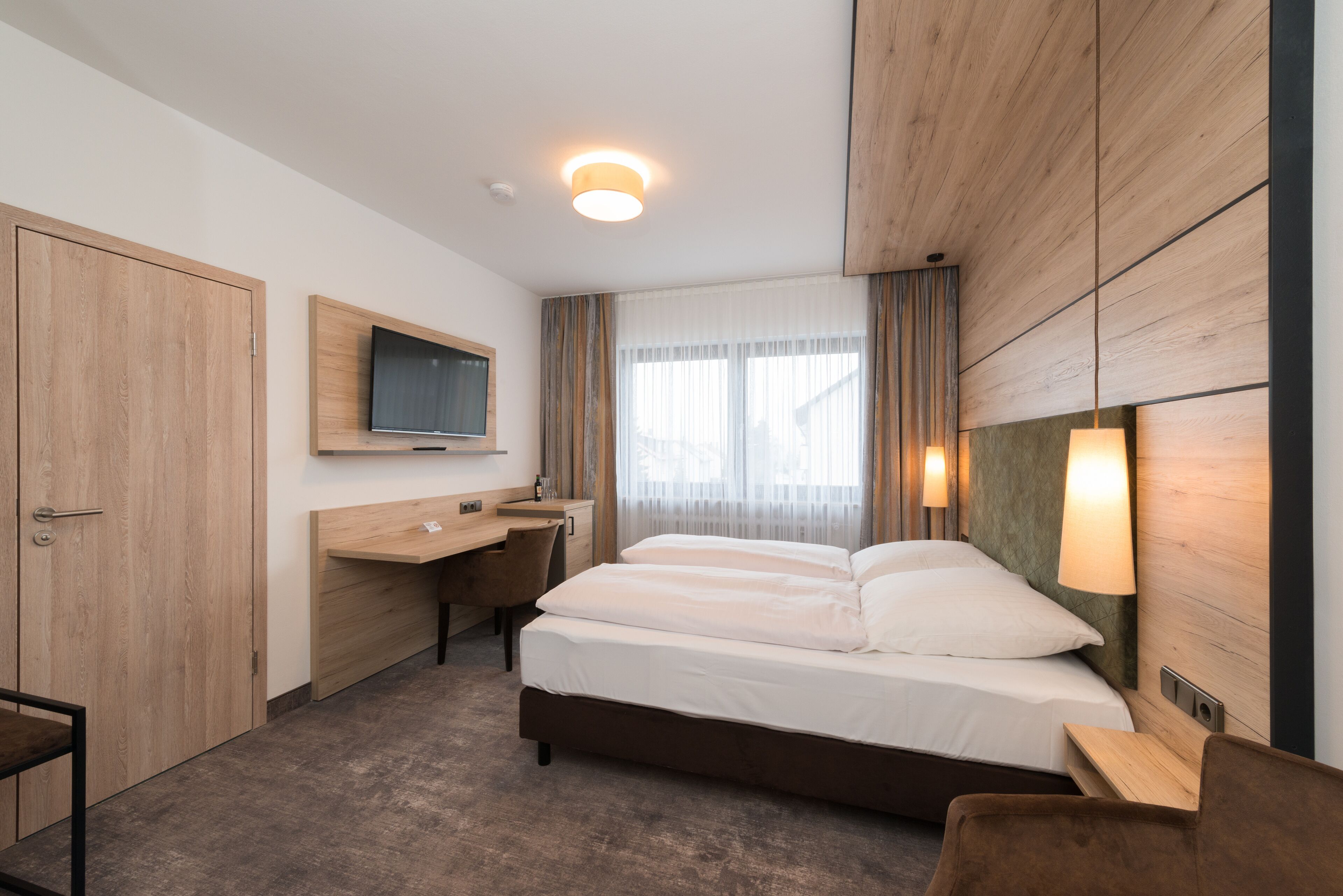A hotel room with a bed, desk, chair, TV, and wooden paneling.