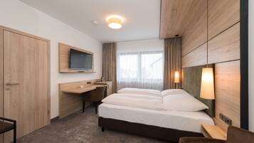A hotel room with a bed, desk, chair, TV, and wooden paneling.