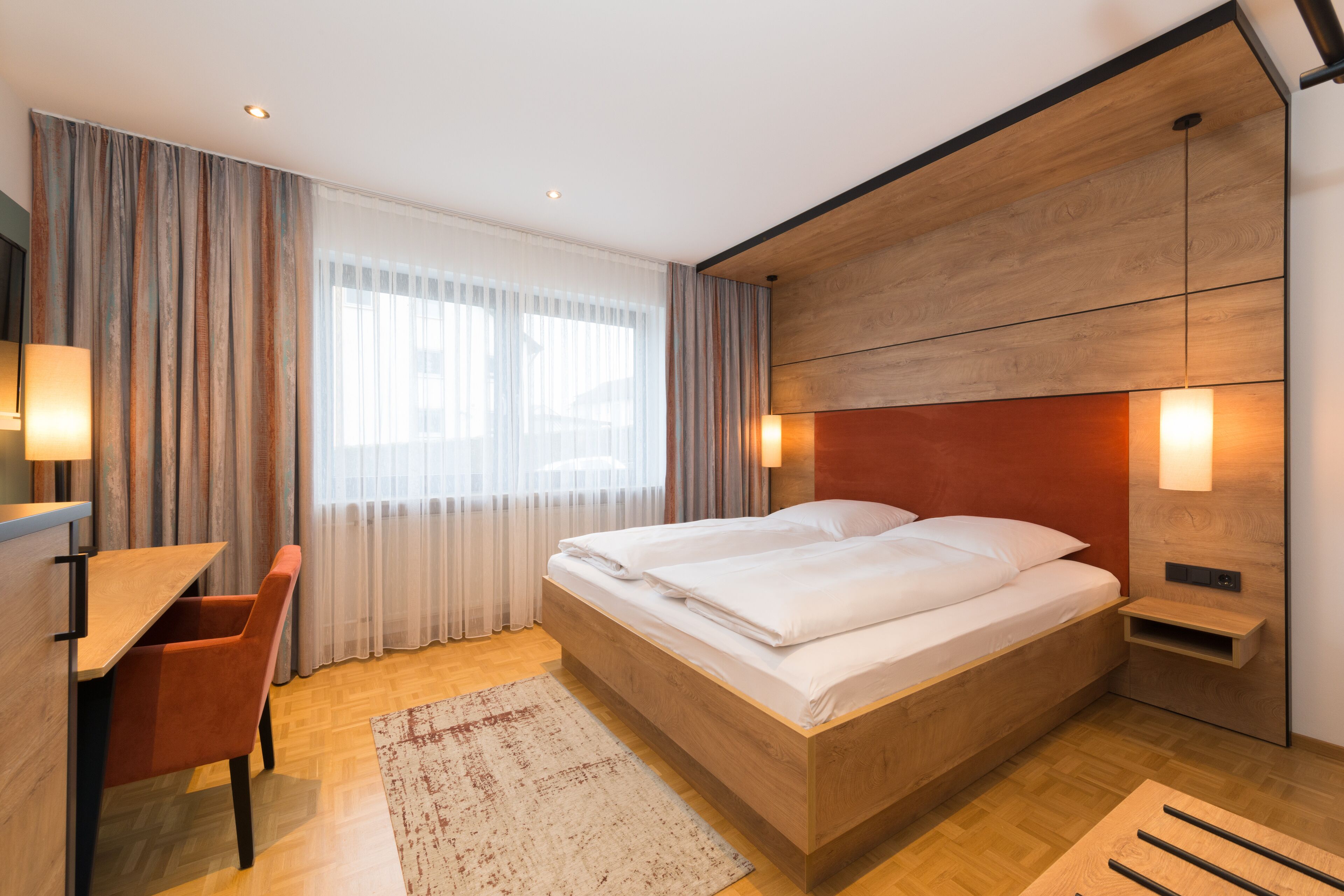 A modern bedroom with a wooden bed, a desk, and a chair.