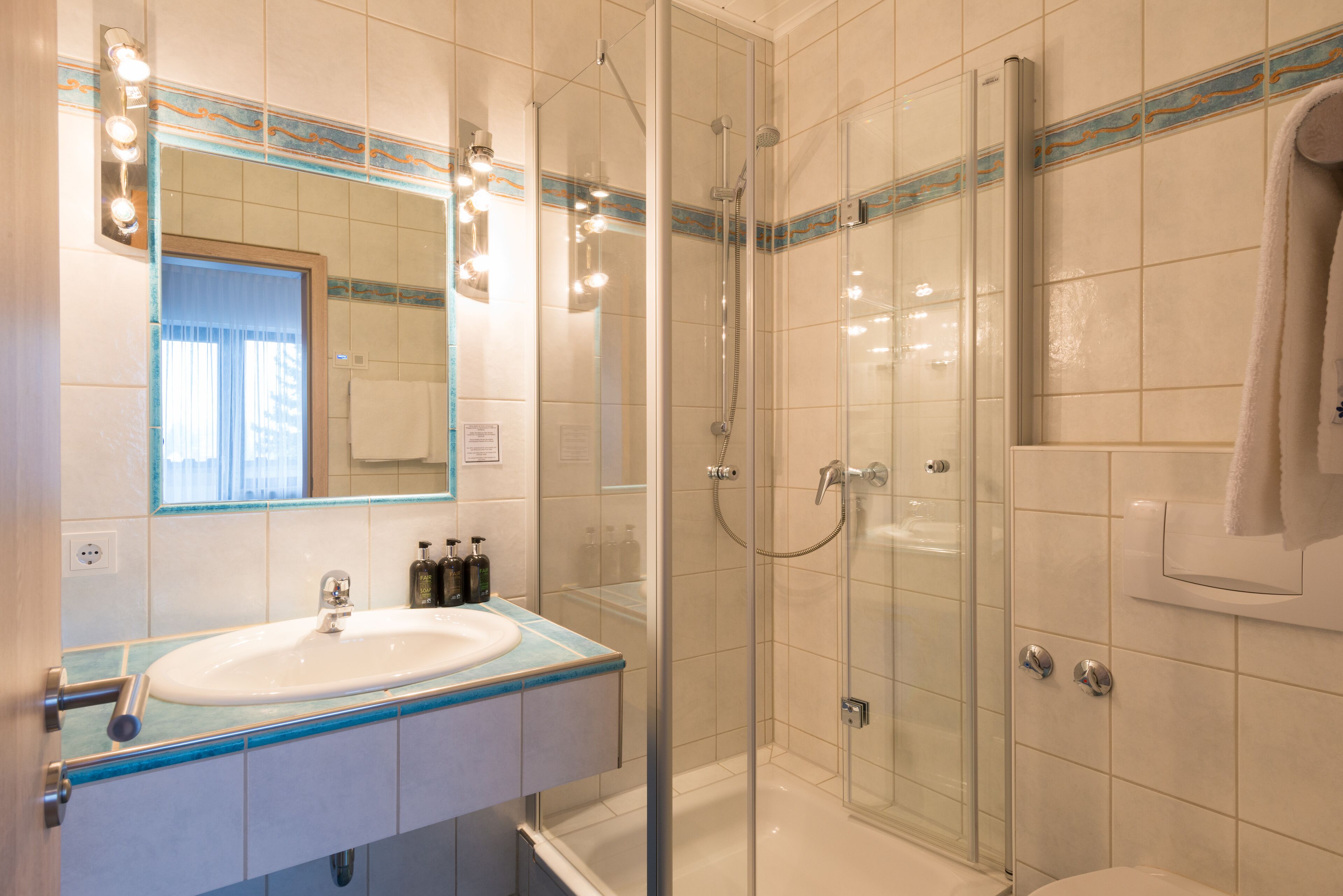 A modern bathroom with a glass-enclosed shower, a sink with a blue countertop, and a mirror with lights above it.