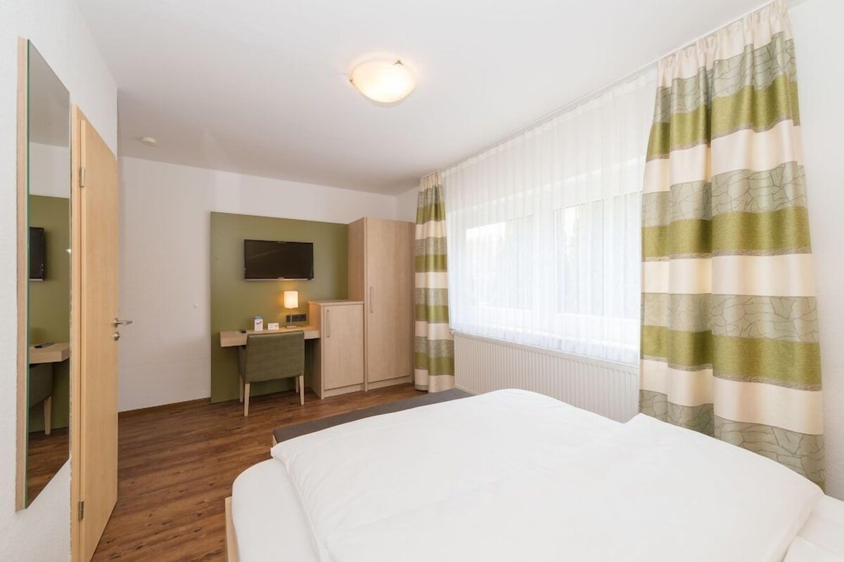 Un dormitorio con una cama, un escritorio, una silla, un televisor y una ventana con cortinas.