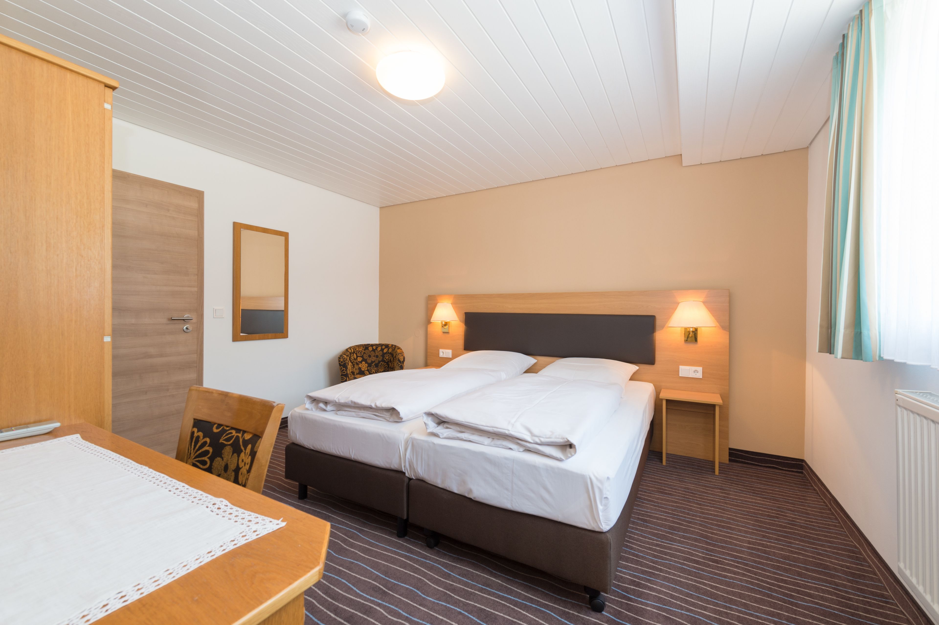 Une chambre d’hôtel comprenant un lit, deux tables de chevet, une chaise, un bureau et un grand miroir.