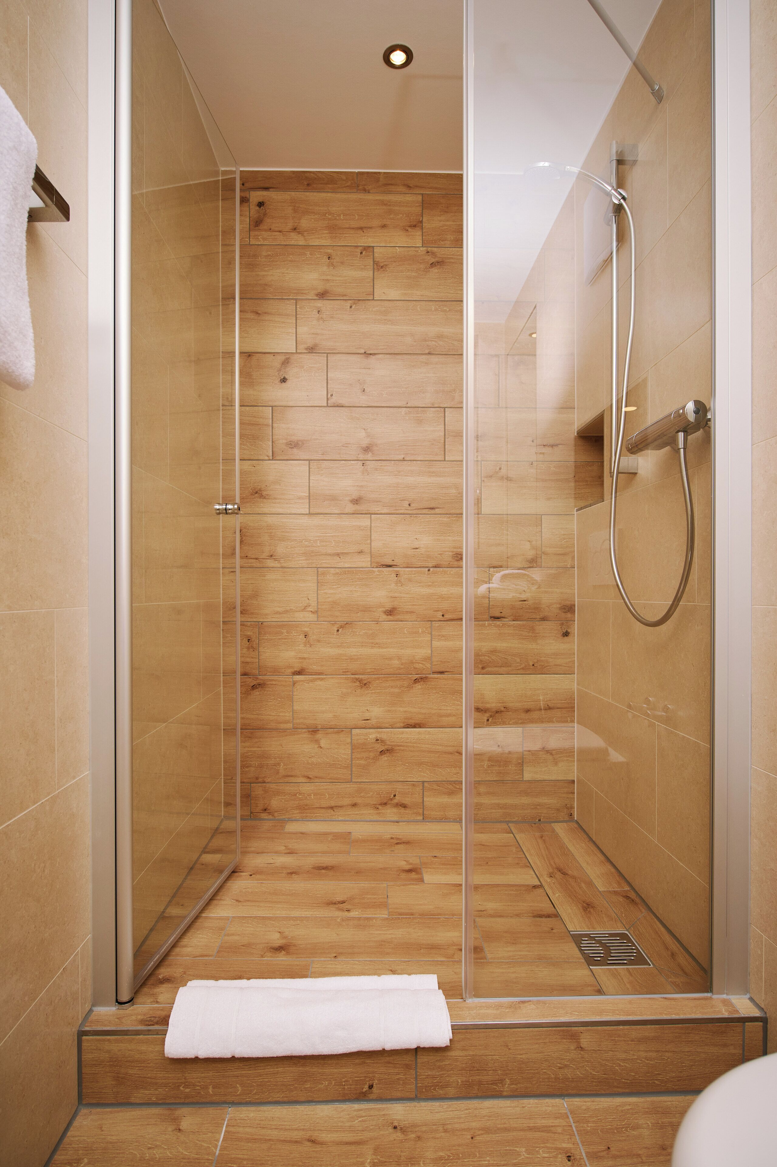 A glass-enclosed shower with wooden flooring and a white towel on the floor.
