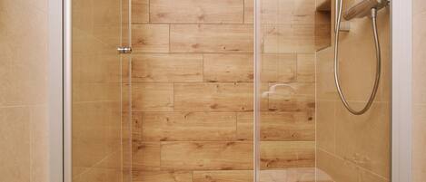 A glass-enclosed shower with wooden flooring and a white towel on the floor.