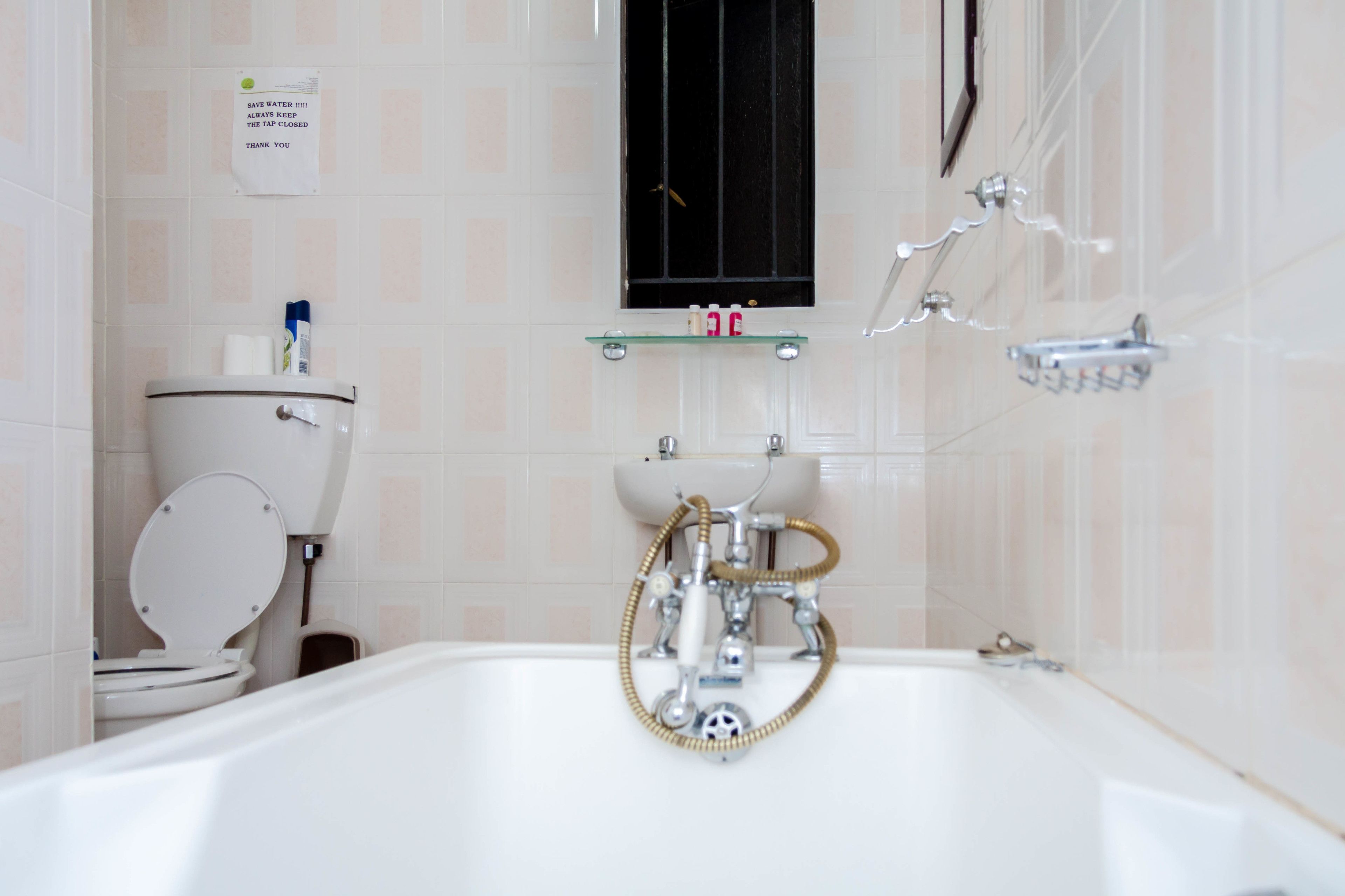 A bathroom with a toilet, sink, and bathtub. There is a sign on the wall and a window above the sink.