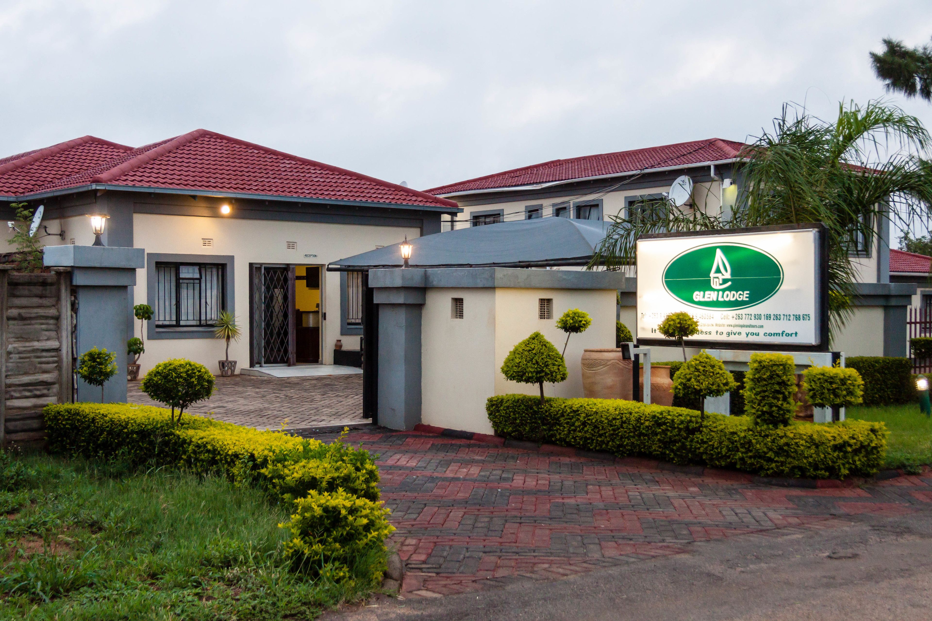 A hotel with a red-tiled roof, a signboard, and well-maintained hedges.