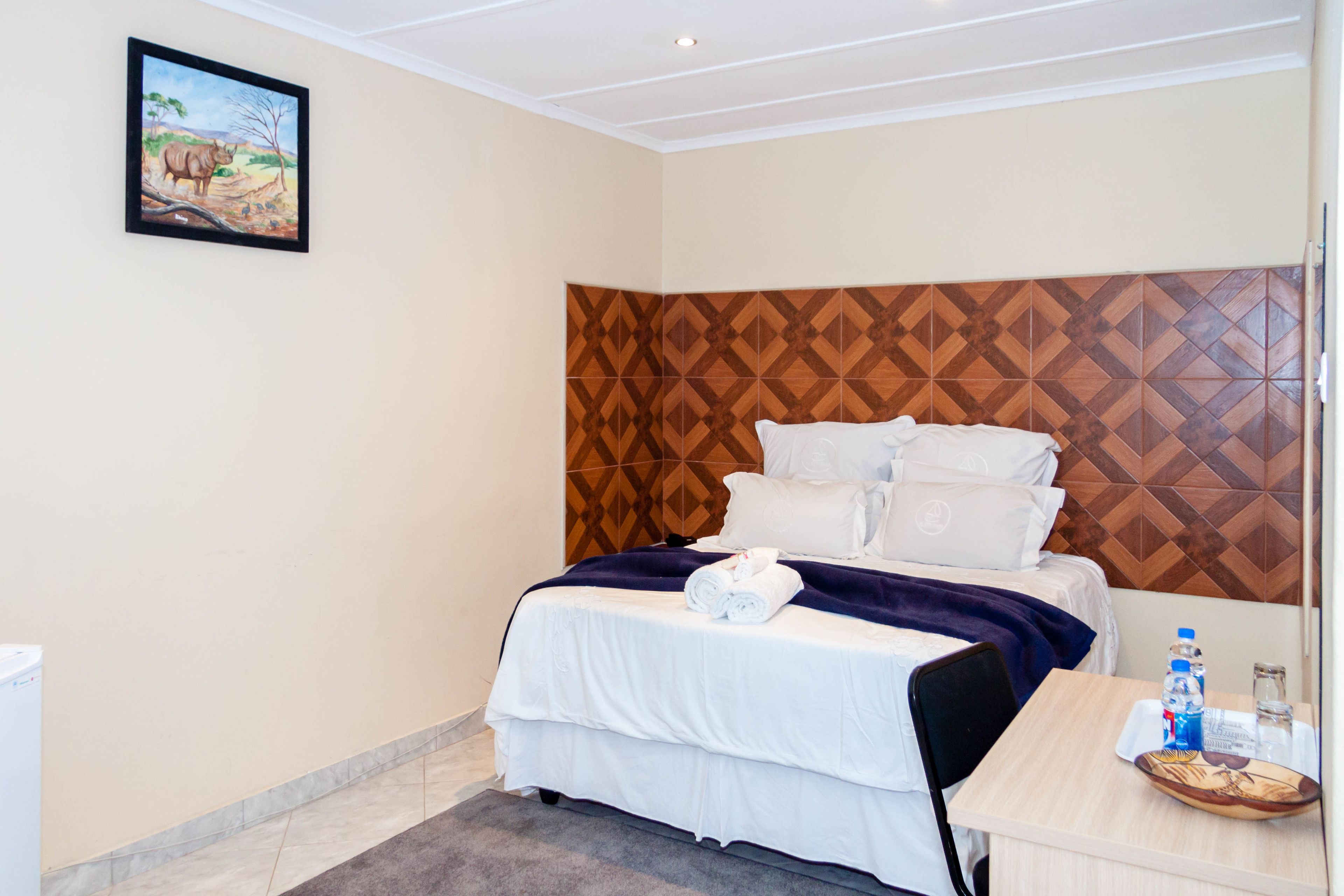 Ein Hotelzimmer mit einem Bett, einem Kopfteil mit geometrischem Muster, einem Nachttisch mit Tablett und einem Bild an der Wand.