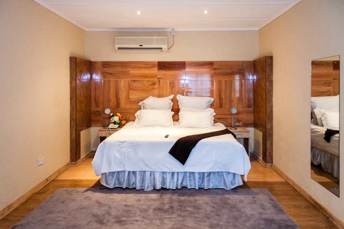 Ein Schlafzimmer mit einem hölzernen Kopfende, einem großen Bett mit weißer Bettwäsche, einem Nachttisch mit Lampe und einem Spiegel an der Wand.