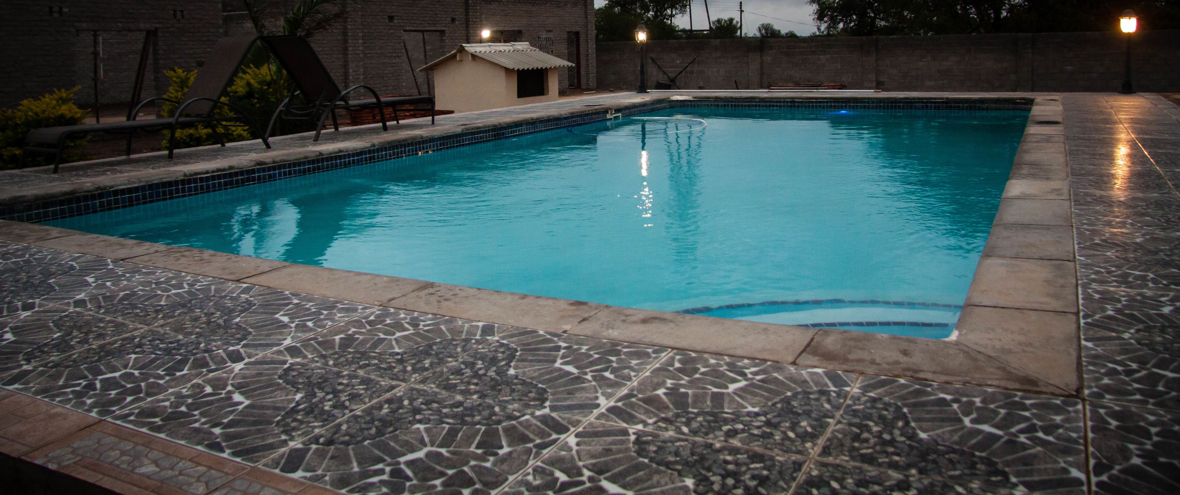 Una piscina con plataforma de azulejos, rodeada por un muro bajo y algunas sillas de descanso.