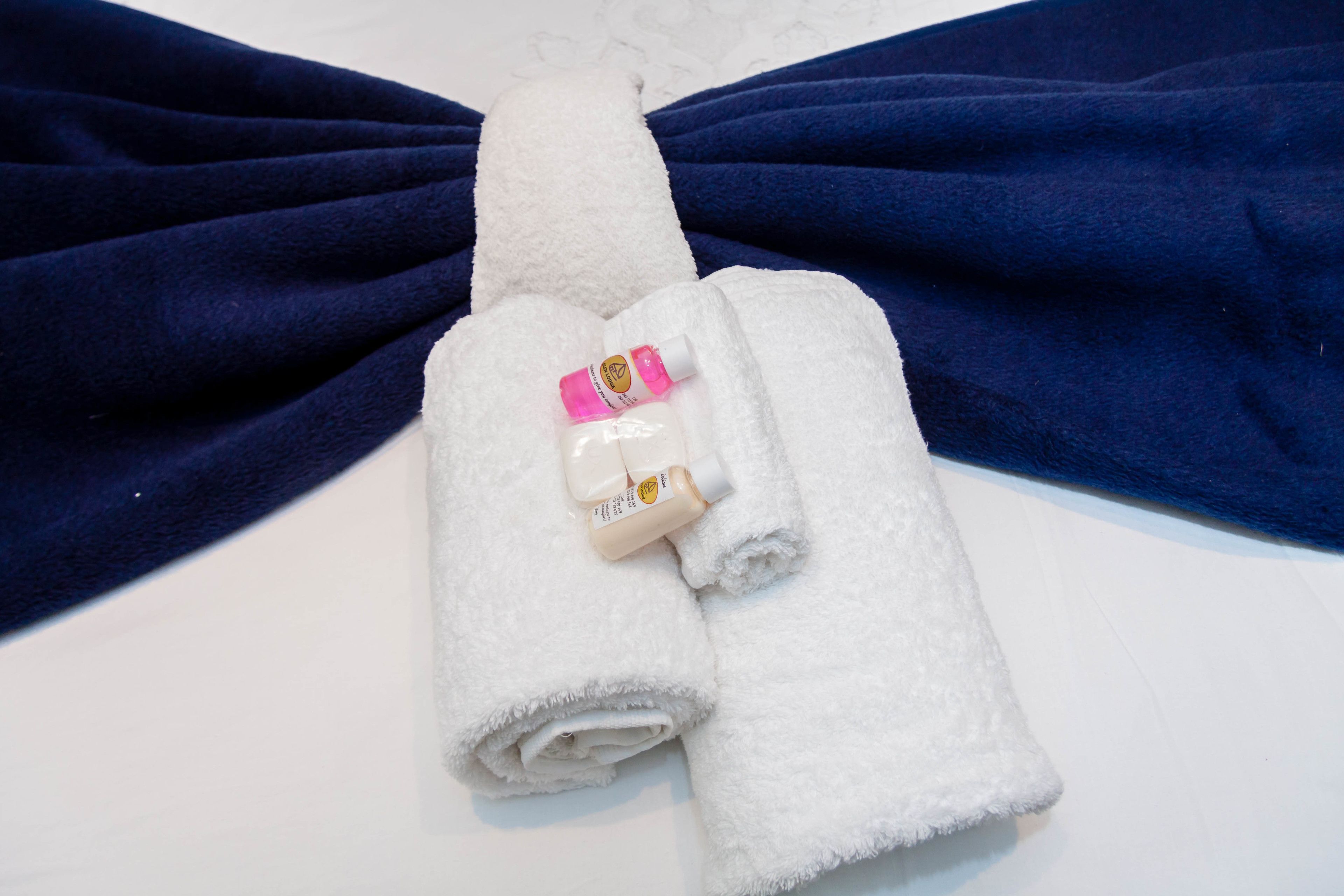 Ein weißes Handtuch liegt gefaltet auf einem blauen Handtuch, zusammen mit einer Lotionflasche und einer kleinen Shampooflasche.