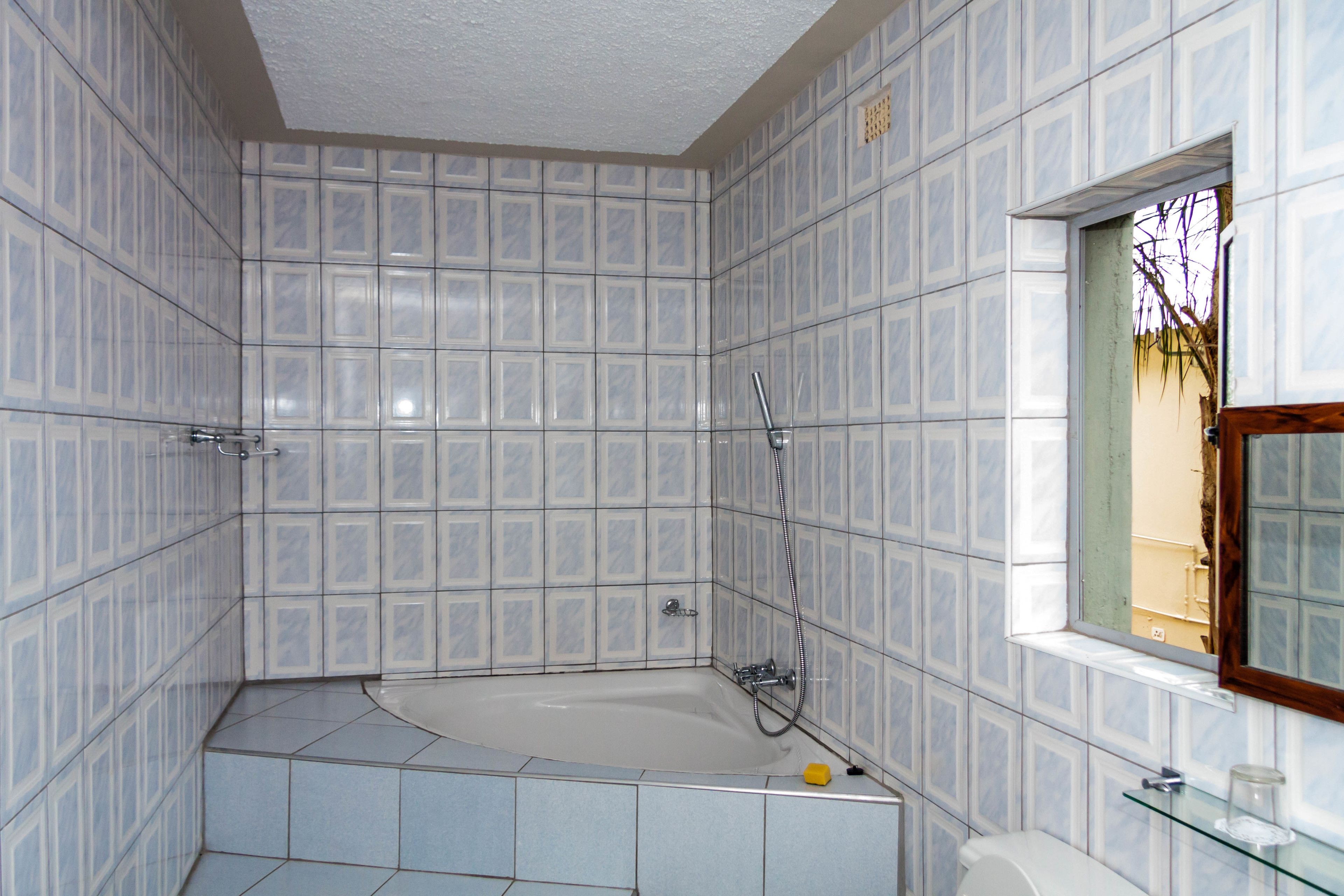 Een badkamer met een bad, betegelde wanden, een raam en een glazen plank.