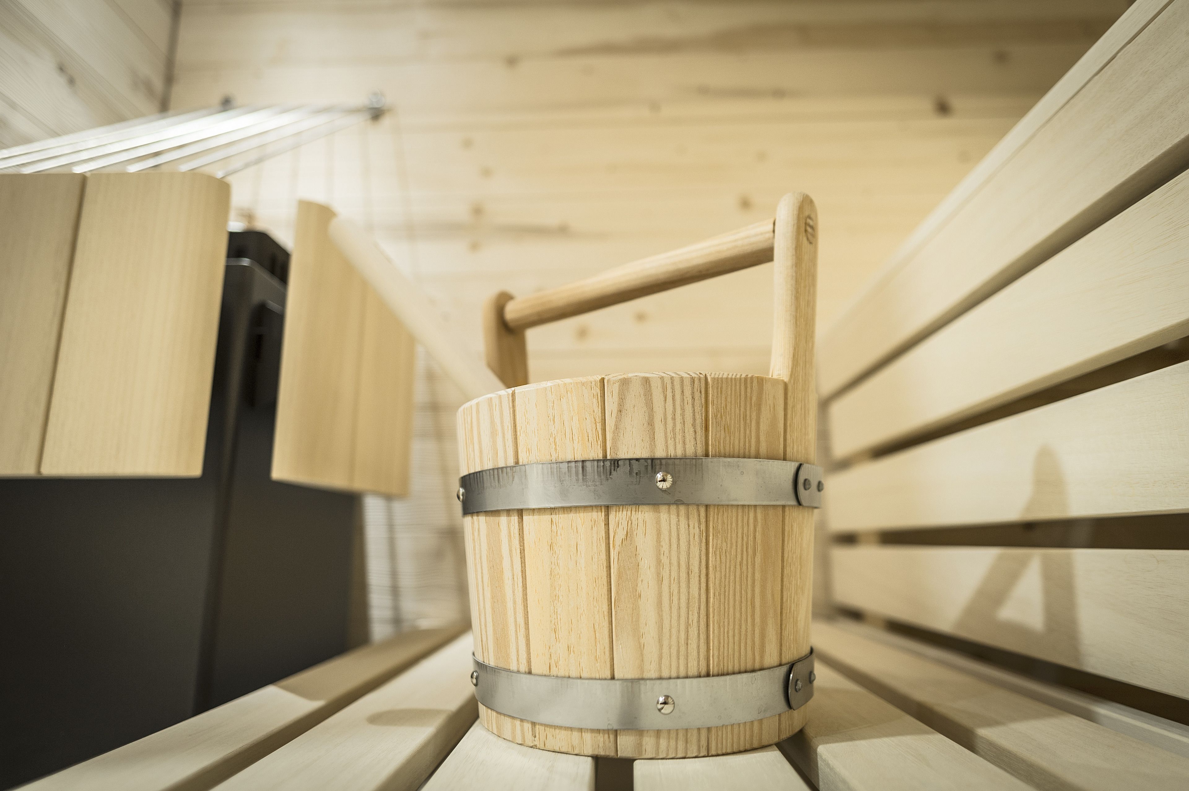 A wooden barrel with metal bands and a handle, placed on a bench in a wooden interior.