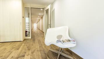A modern hallway with wooden flooring, a white chair with magazines, and a fire extinguisher on the left.
