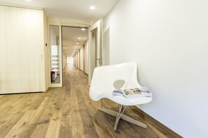A modern hallway with wooden flooring, a white chair with magazines, and a fire extinguisher on the left. - alpen select apartments Kleinwalsertal (Mittelberg)