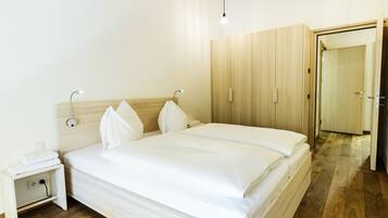 A neatly made bed with white linens, a bedside table with a lamp, and wooden wardrobe with a door.