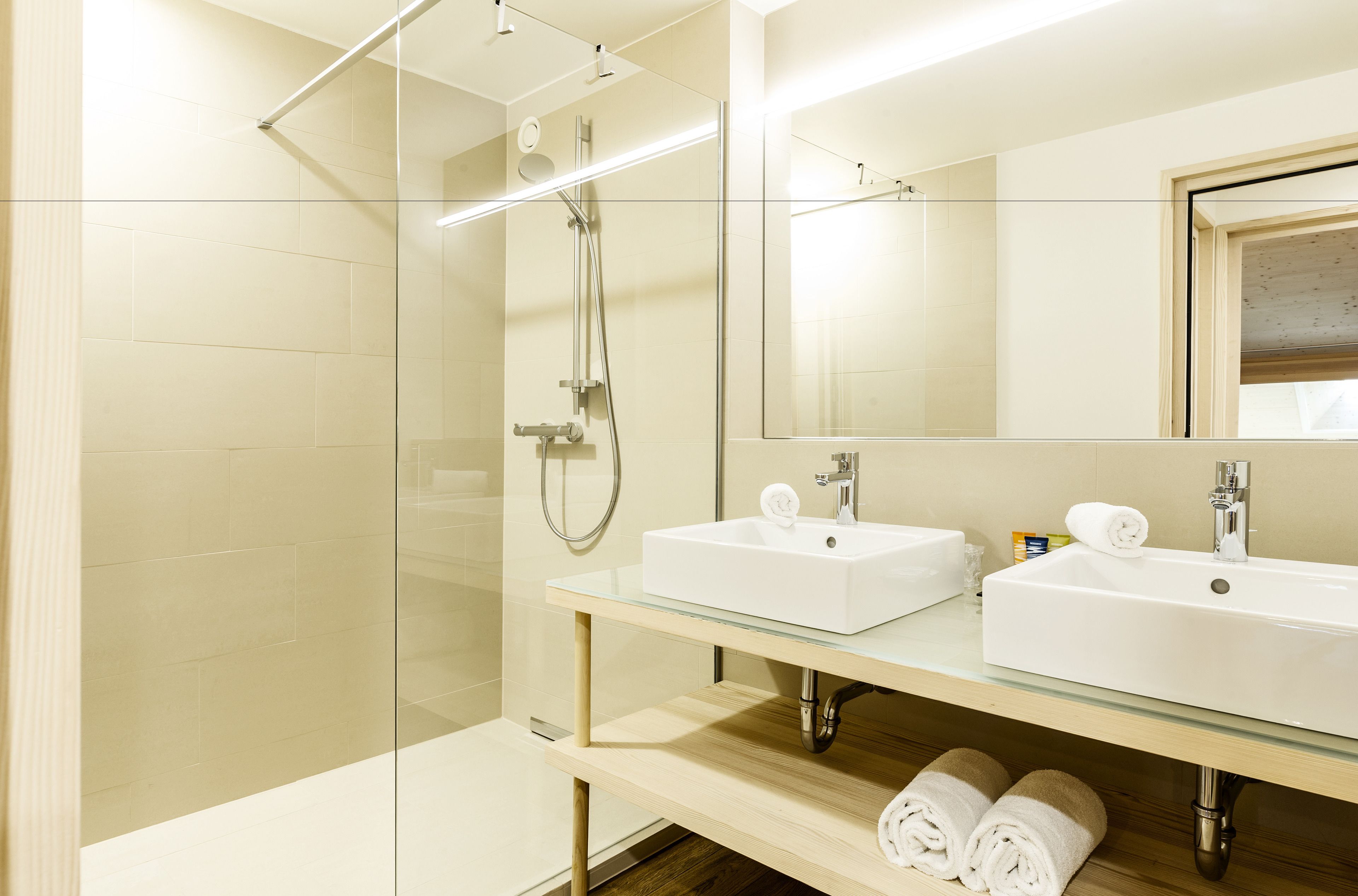 Un bagno moderno con cabina doccia in vetro, due lavabi e uno specchio grande.