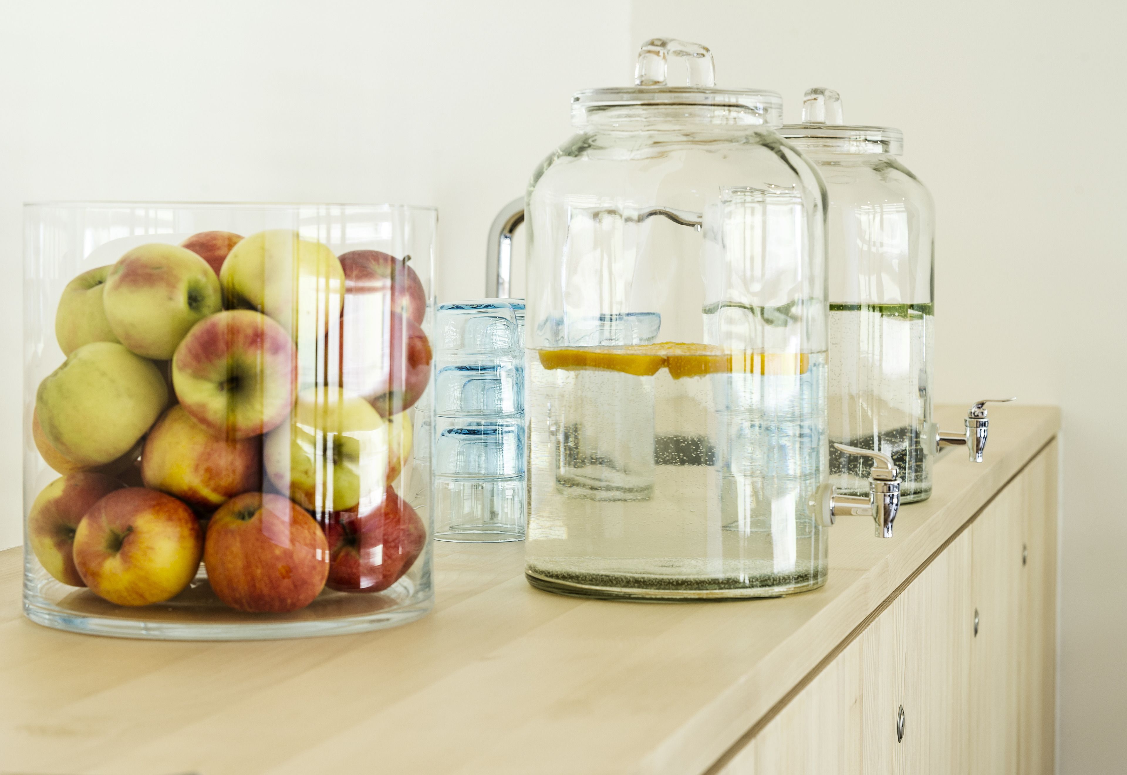 Un comptoir de cuisine sur lequel se trouve un bocal en verre rempli de pommes et deux autres bocaux en verre contenant de l’eau et des tranches de citron.