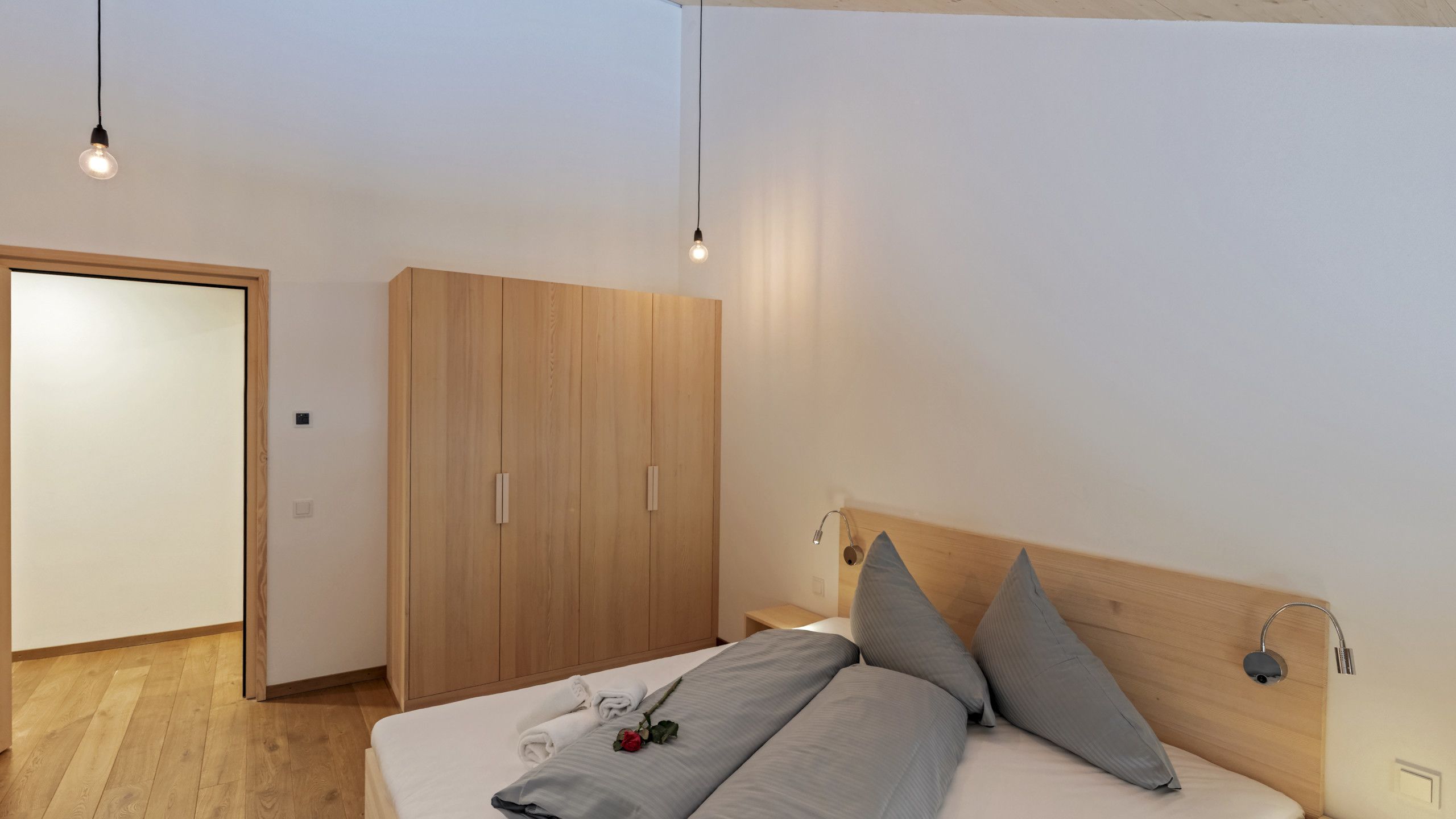 Un dormitorio moderno con un armario de madera, una cama con ropa de cama gris y dos lámparas de noche.