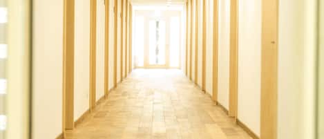 A long, narrow hallway with wooden floors and walls, leading to a bright exit.