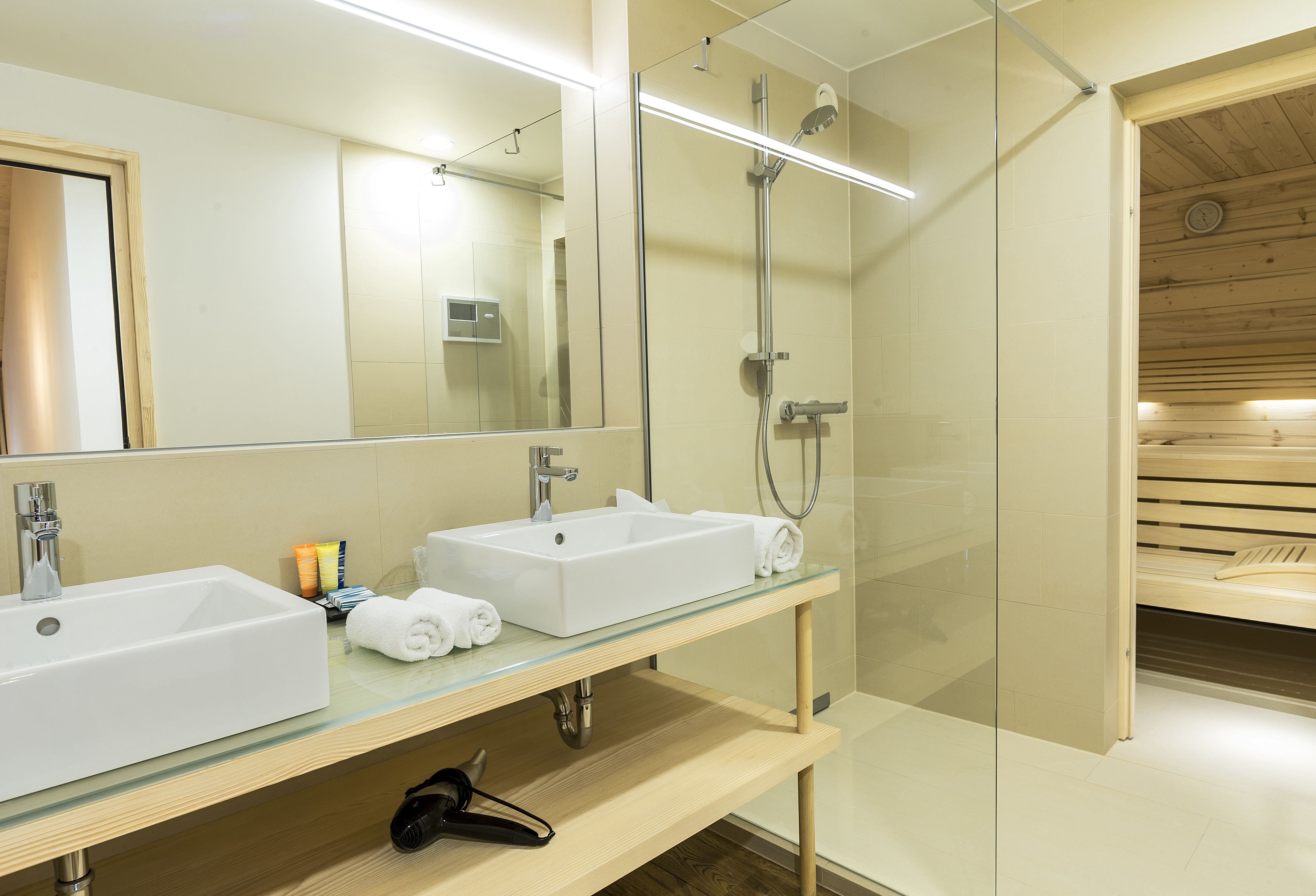Un bagno moderno con due lavandini, cabina doccia in vetro e una panca in legno.