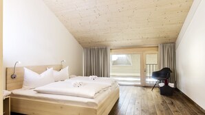 A bedroom with a wooden ceiling, a large bed with white bedding, a bedside table, and a chair. - alpen select apartments Kleinwalsertal (Mittelberg)