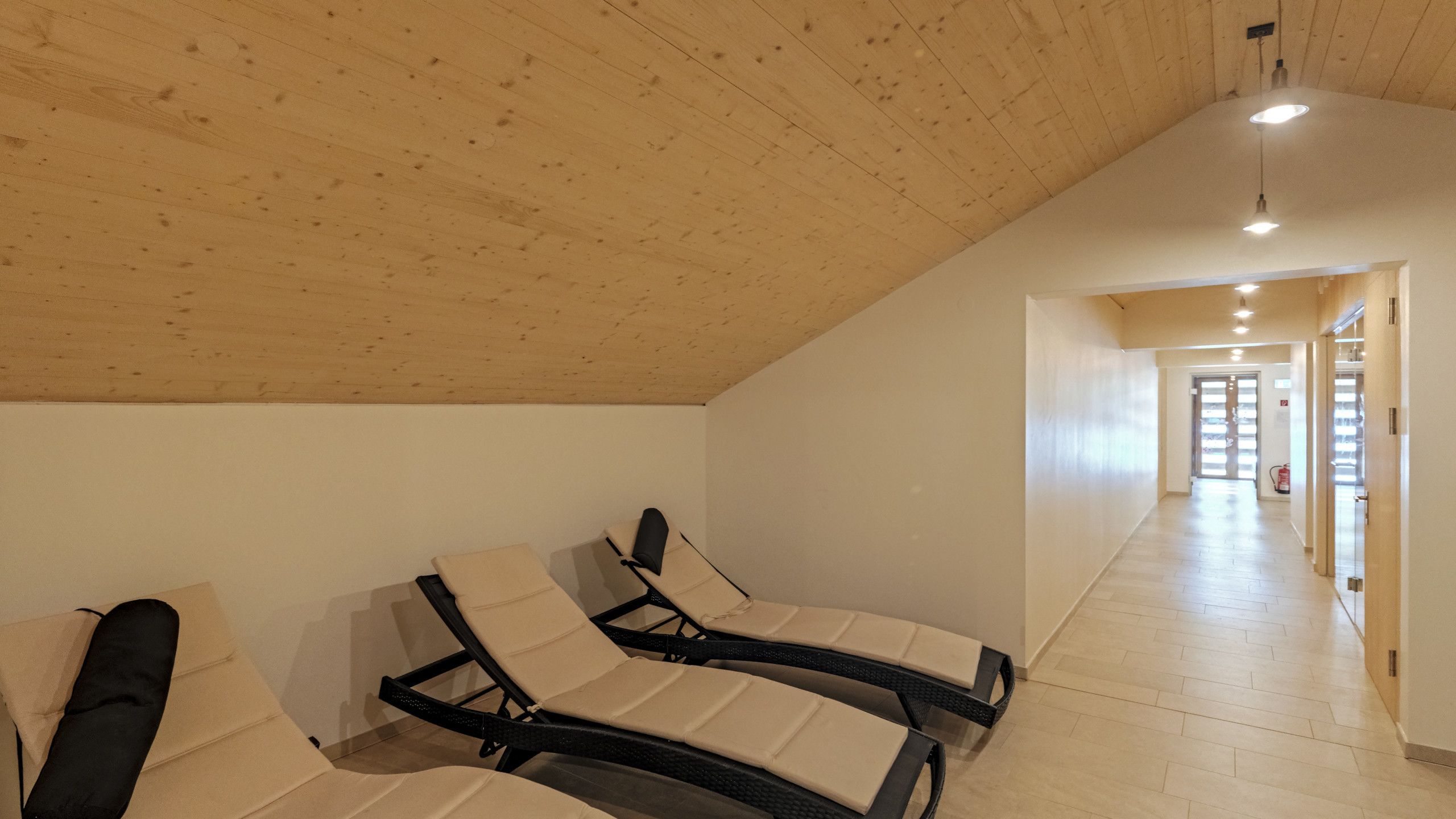 Amplia habitación con techo y paredes de madera, con dos sillones reclinables y un pasillo que conduce a una puerta.