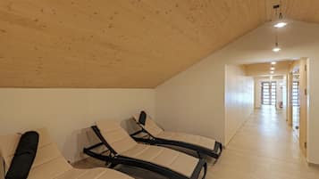 Amplia habitación con techo y paredes de madera, con dos sillones reclinables y un pasillo que conduce a una puerta.