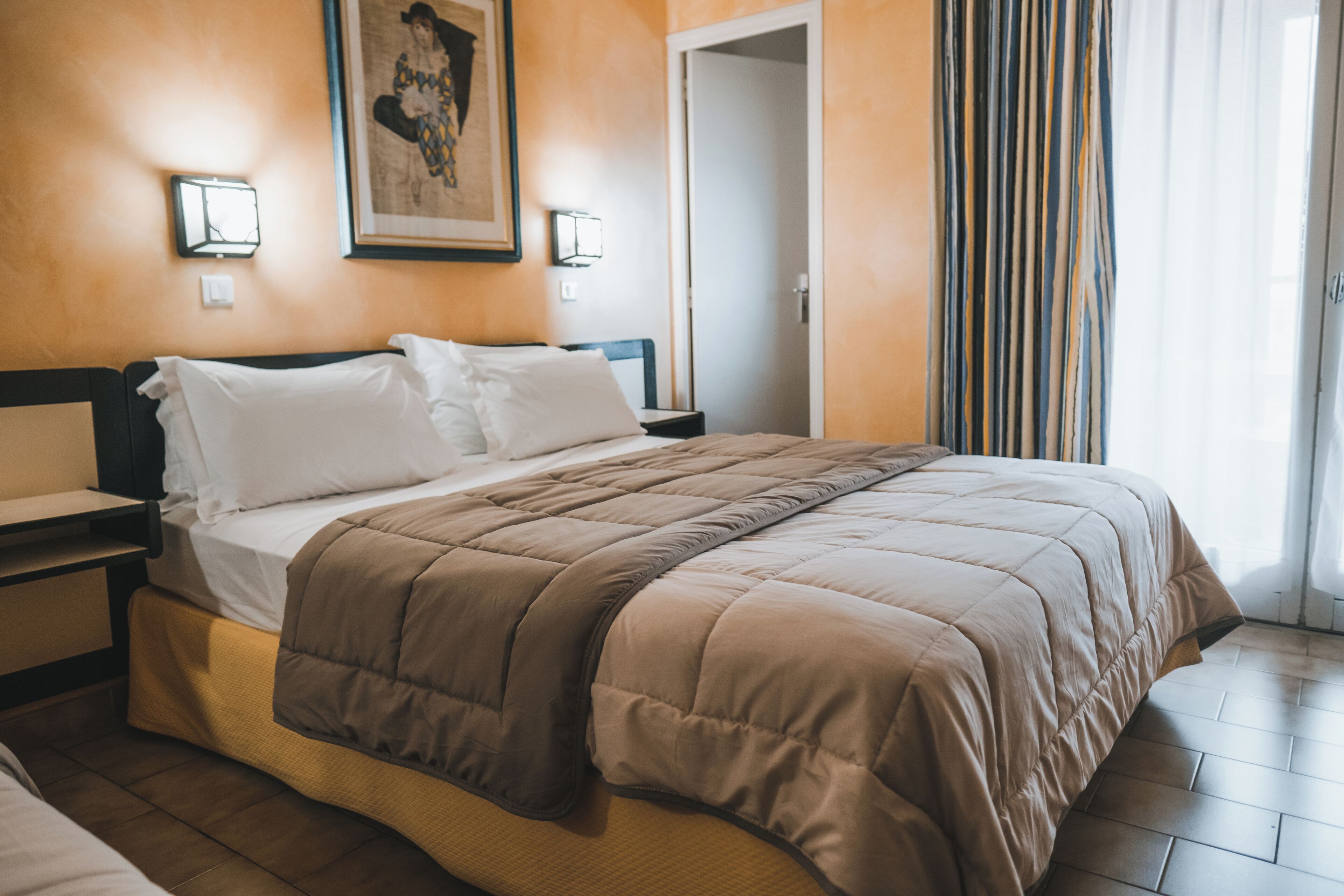 Een hotelkamer met een bed, nachtkastjes, een schilderij en een deur.