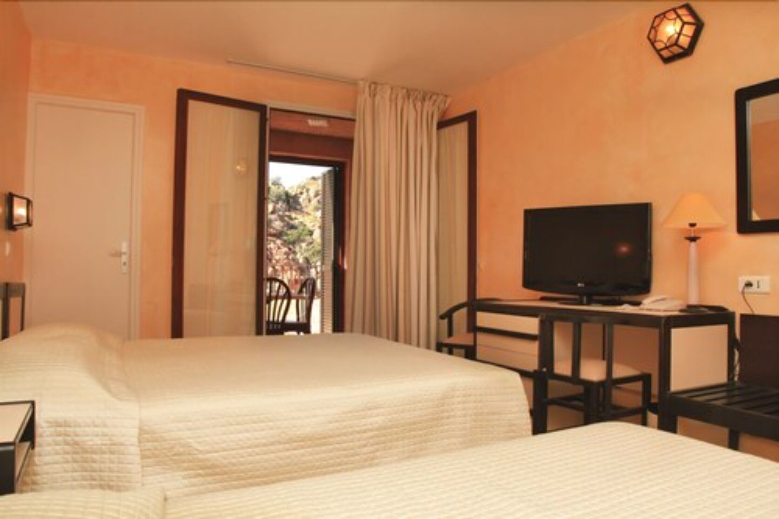 A hotel room with two beds, a TV, a desk, and a view of the outdoors.