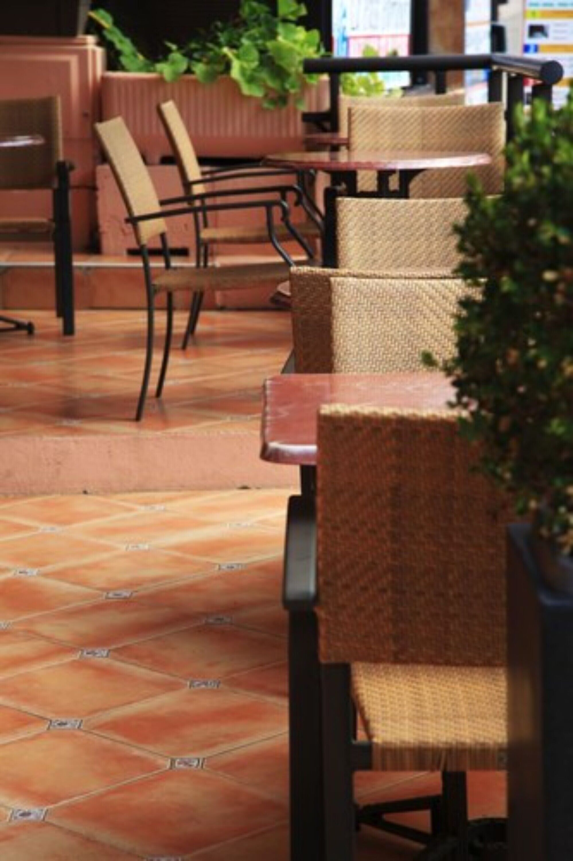 An outdoor seating area with wicker chairs and tables, a tiled floor, and potted plants.