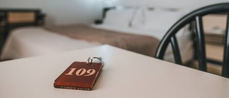 Un llavero con el número 109 sobre una mesa blanca en una habitación con cama y silla.