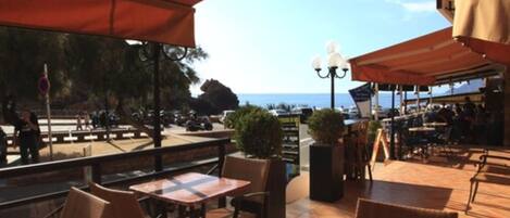 Un café al aire libre con mesas y sillas, vistas al mar y una zona de estar cubierta.