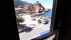 A coastal town with a rocky hill, a road with cars, and boats in the water. - Hôtel le Subrini (Ota)