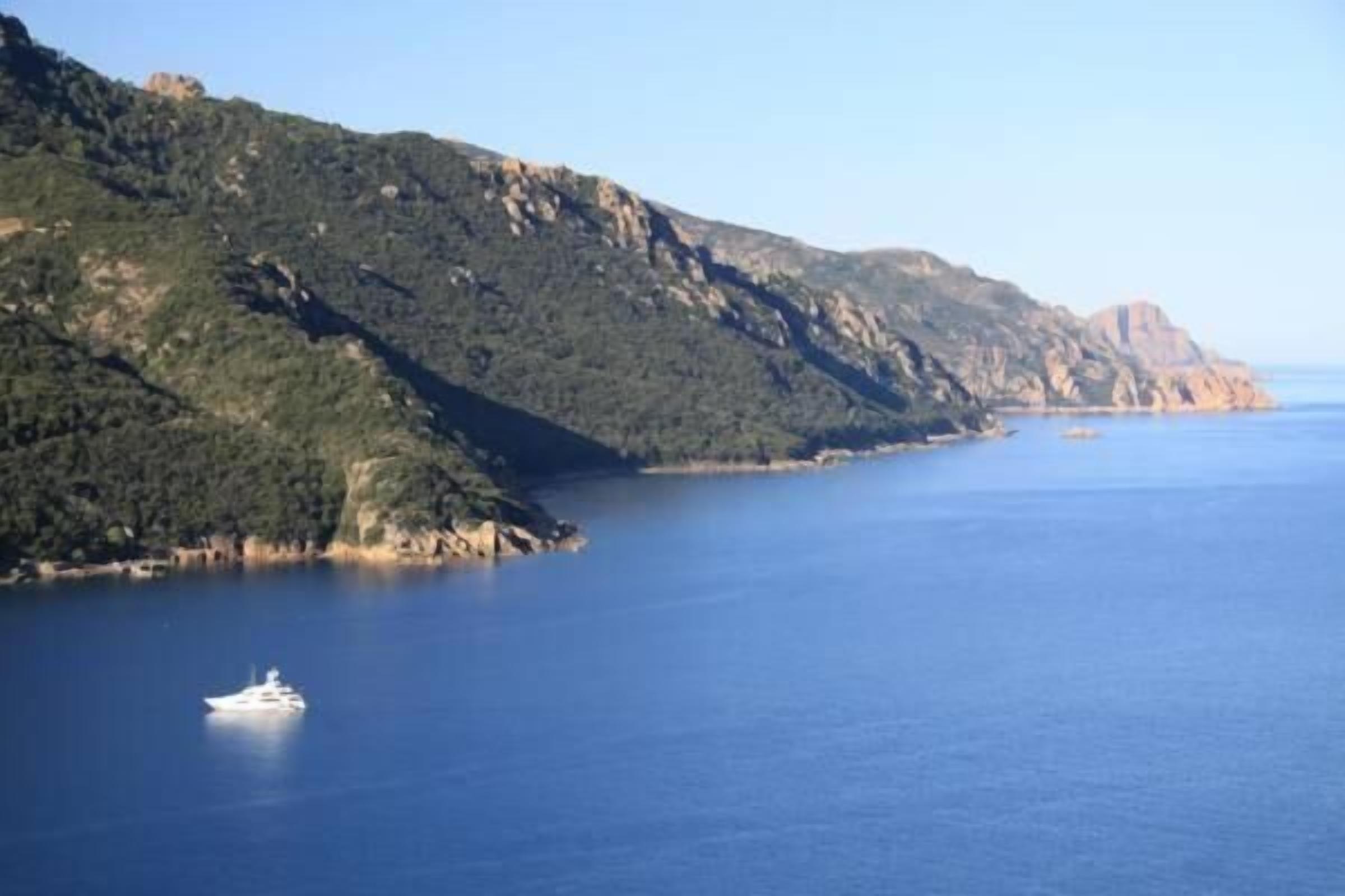 Un paisaje costero con un yate en el agua y acantilados rocosos al fondo.