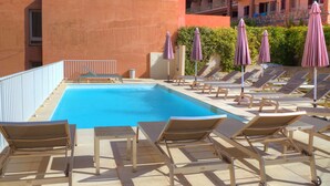 A poolside area with sun loungers and umbrellas, a clear blue pool, and a building with balconies in the background. - Hôtel Idéal (Ota)