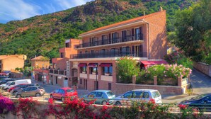 A hotel with a red roof, multiple balconies, and a parking lot with several cars. - Hôtel Idéal (Ota)