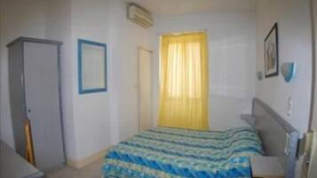 A bedroom with a bed, a wardrobe, a window with yellow curtains, and a wall-mounted air conditioner.