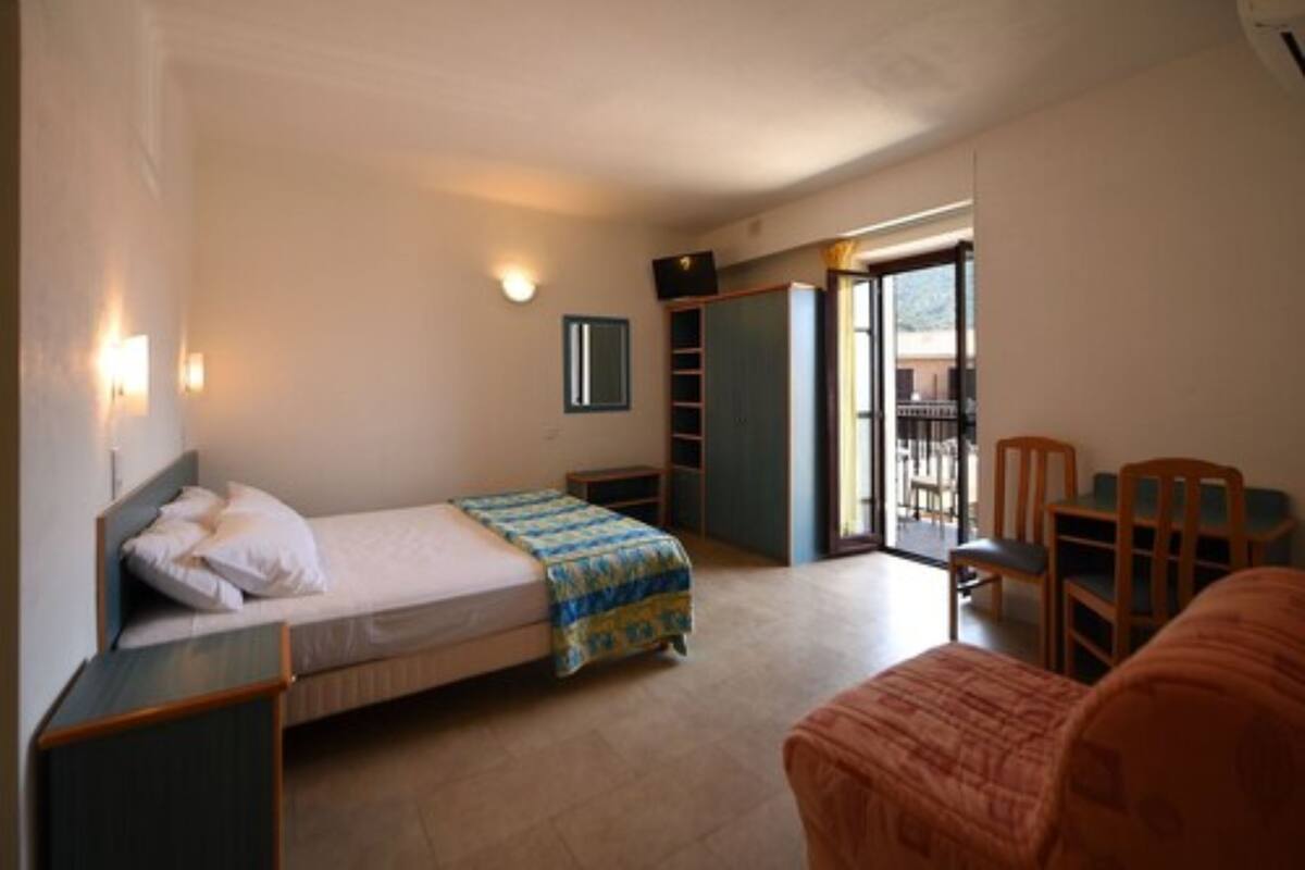 A bedroom with a bed, a chair, a small table, a wardrobe, and a balcony.