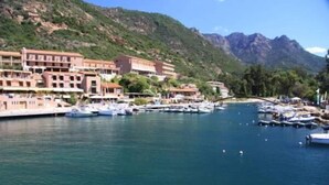 A marina with boats docked, a building with multiple floors, and a mountainous backdrop. - Hôtel Idéal (Ota)