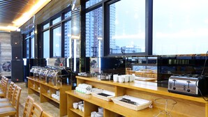 Un montaje tipo bufé con varias estaciones de servicio, un ventanal con vistas a la ciudad y una zona de cocina con un tostador.