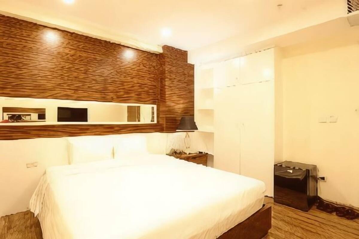 Ein Hotelzimmer mit einem großen Bett, einem Holzkopfteil, einem Flachbildfernseher, einem Nachttisch mit einer Lampe und einem Koffer.