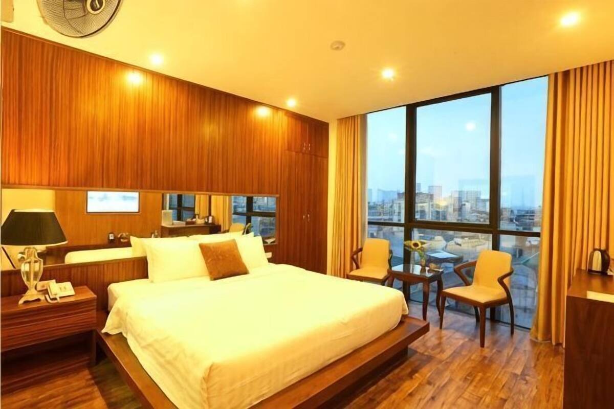 Ein Hotelzimmer mit einem großen Bett, einem Schreibtisch, einem Stuhl, einem Ventilator und Blick auf die Stadt.