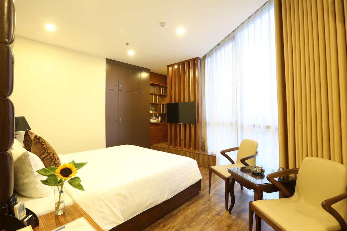 Ein Hotelzimmer mit einem großen Bett, einem Schreibtisch mit Stuhl, einem Fernseher und einem Fenster mit Vorhängen.