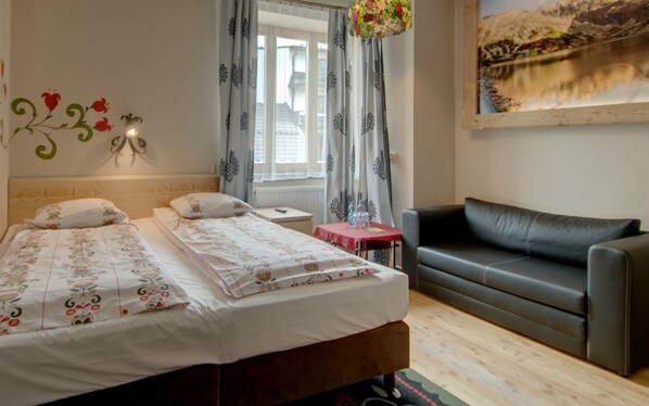 A bedroom with a bed, a small table, a couch, and a window with curtains.